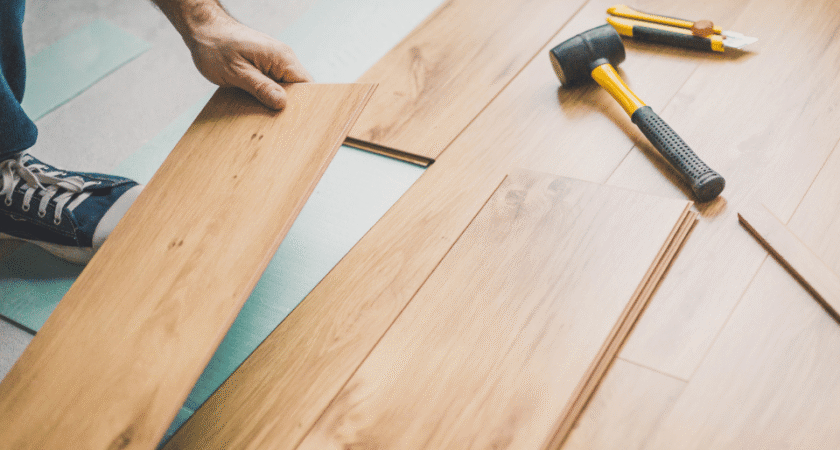 Installer laying wood plank flooring with a hammer