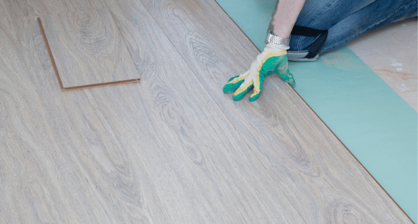 Installer laying light wood-look laminate flooring over underlayment