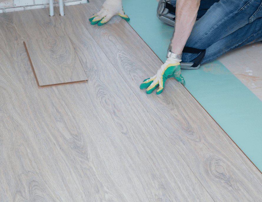 Installer laying light wood-look laminate flooring over underlayment